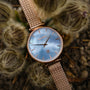 "Chitchat", a wristwatch featuring nacre face and rose gold accents, showcased in a natural setting.