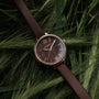 "Shirin" watch with a walnut dial and rose gold accents, set against lush green leaves for an elegant natural style.