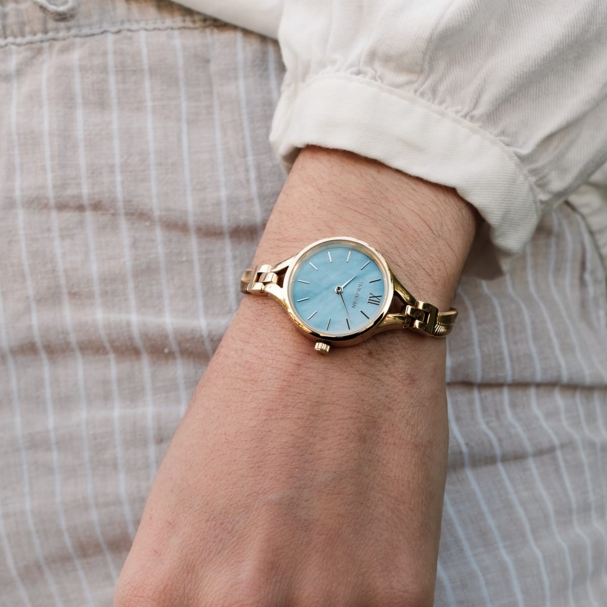 "Shesha" watch, featuring a nacre dial and gold-tone design, elegantly styled on a wrist.