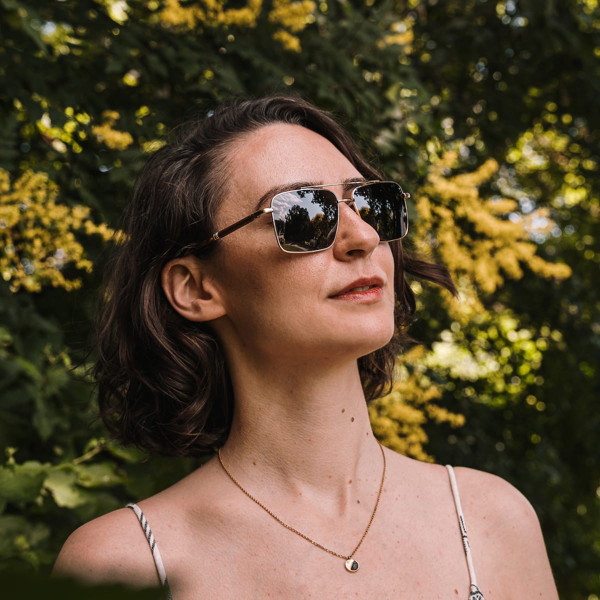 "The Talisman" sunglasses, featuring a walnut and matte gold design, worn stylishly outdoors.