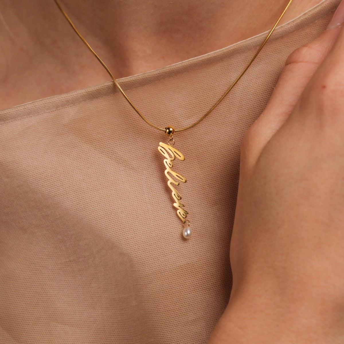 "Believe-Charm" necklace, a gold charm with a pearl accent and a sleek script design.