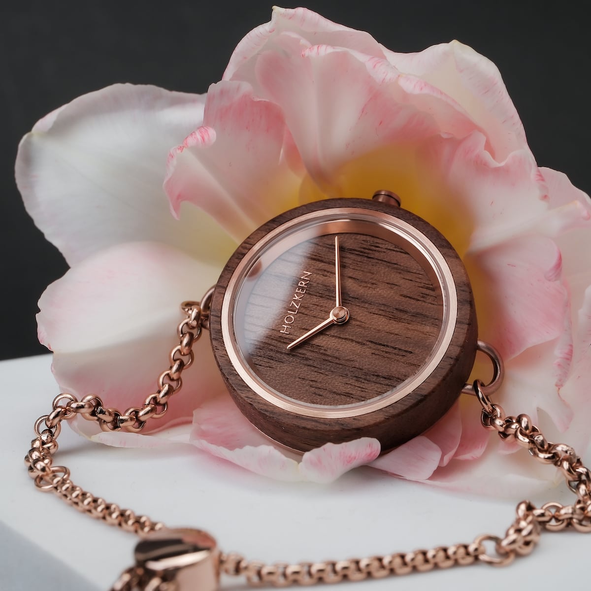 "Leave" watch with a Walnut finish and rose gold accents, set against a soft pink flower backdrop.