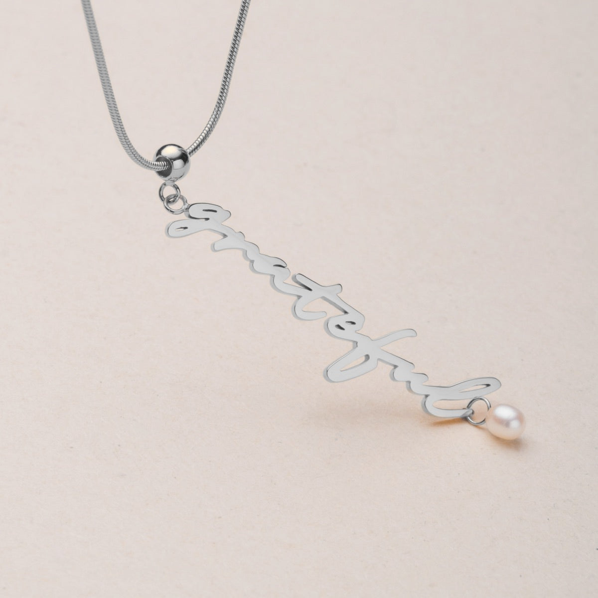 "Grateful-Charm" necklace with a silver script design and pearl accent.