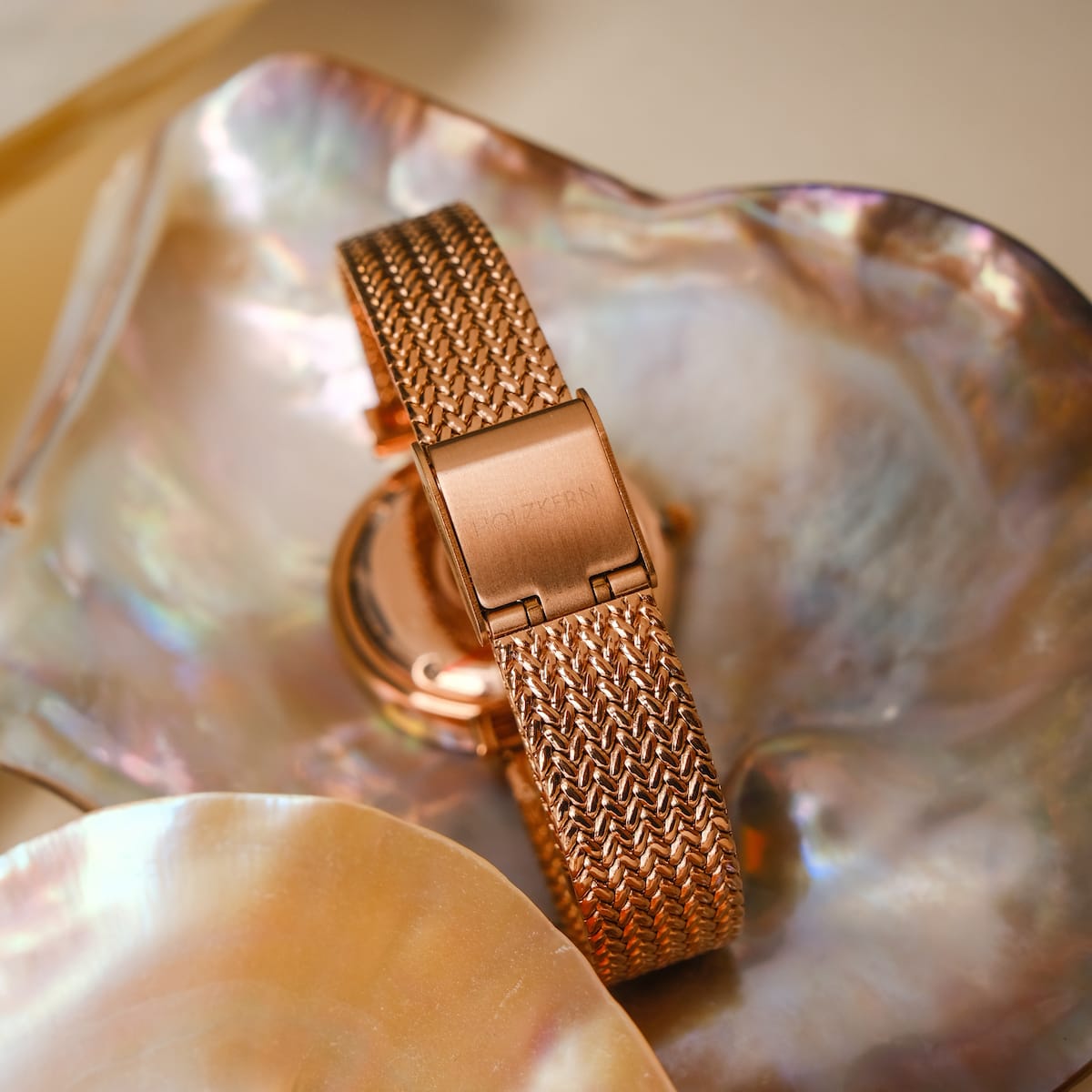 "Chitchat" watch featuring a rose gold mesh band on a nacre backdrop.