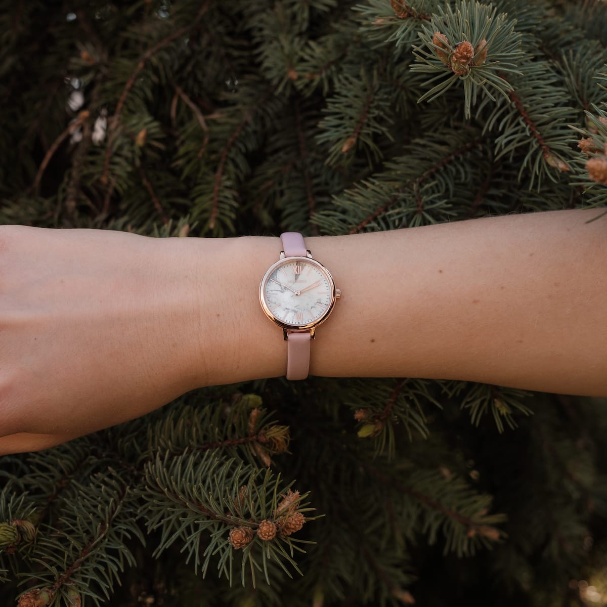 "Alva" watch with a marble face and rose gold accents, featuring a pink strap against a natural green backdrop.