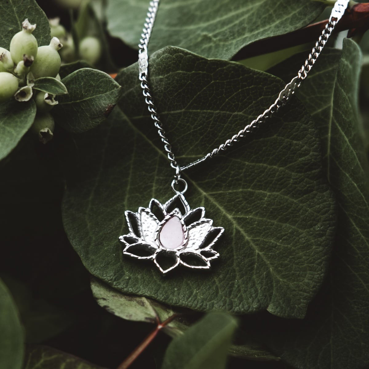 "Balance Necklace", a stylish necklace with a silver lotus and marble-like center, resting on a leafy background.