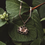 "Balance Necklace" necklace features a delicate walnut and rose gold design, styled elegantly against green foliage.