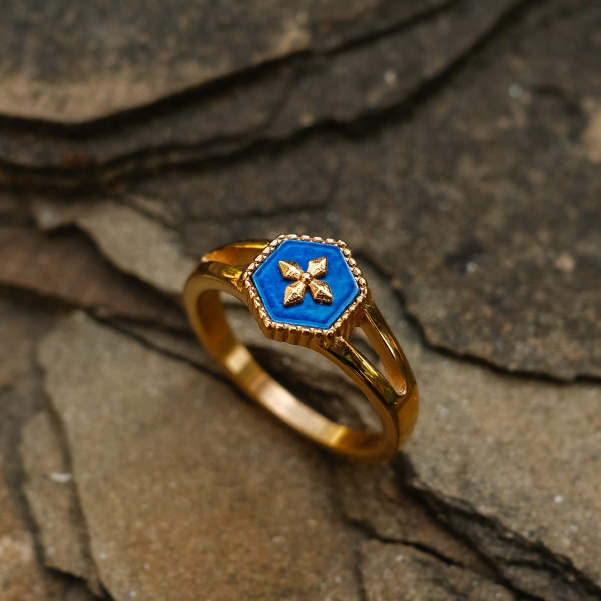 "Spectral Ring": A gold ring featuring a blue nacre centerpiece with an intricate design, set against a natural stone background.