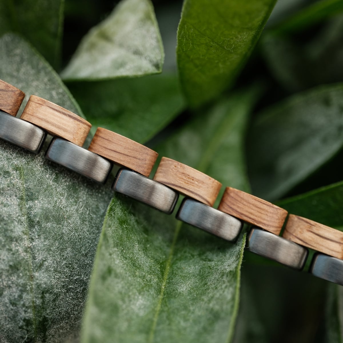 "Duet" bracelet featuring oak wood and gray metal in a natural setting with leaves.