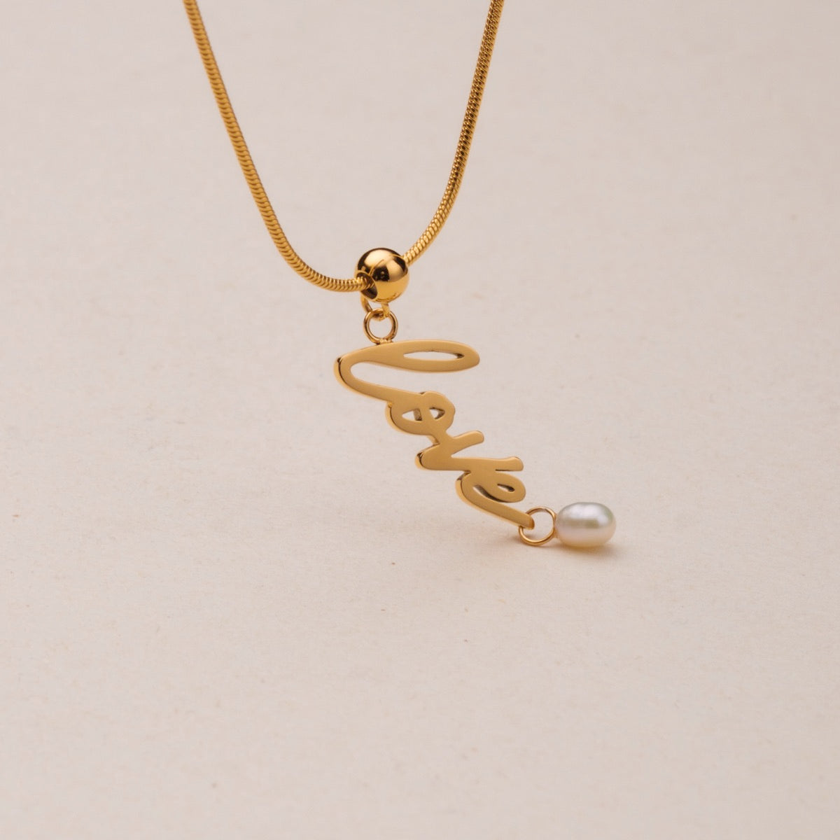 "Love-Charm" necklace featuring elegant gold chain and love charm with pearl accent.
