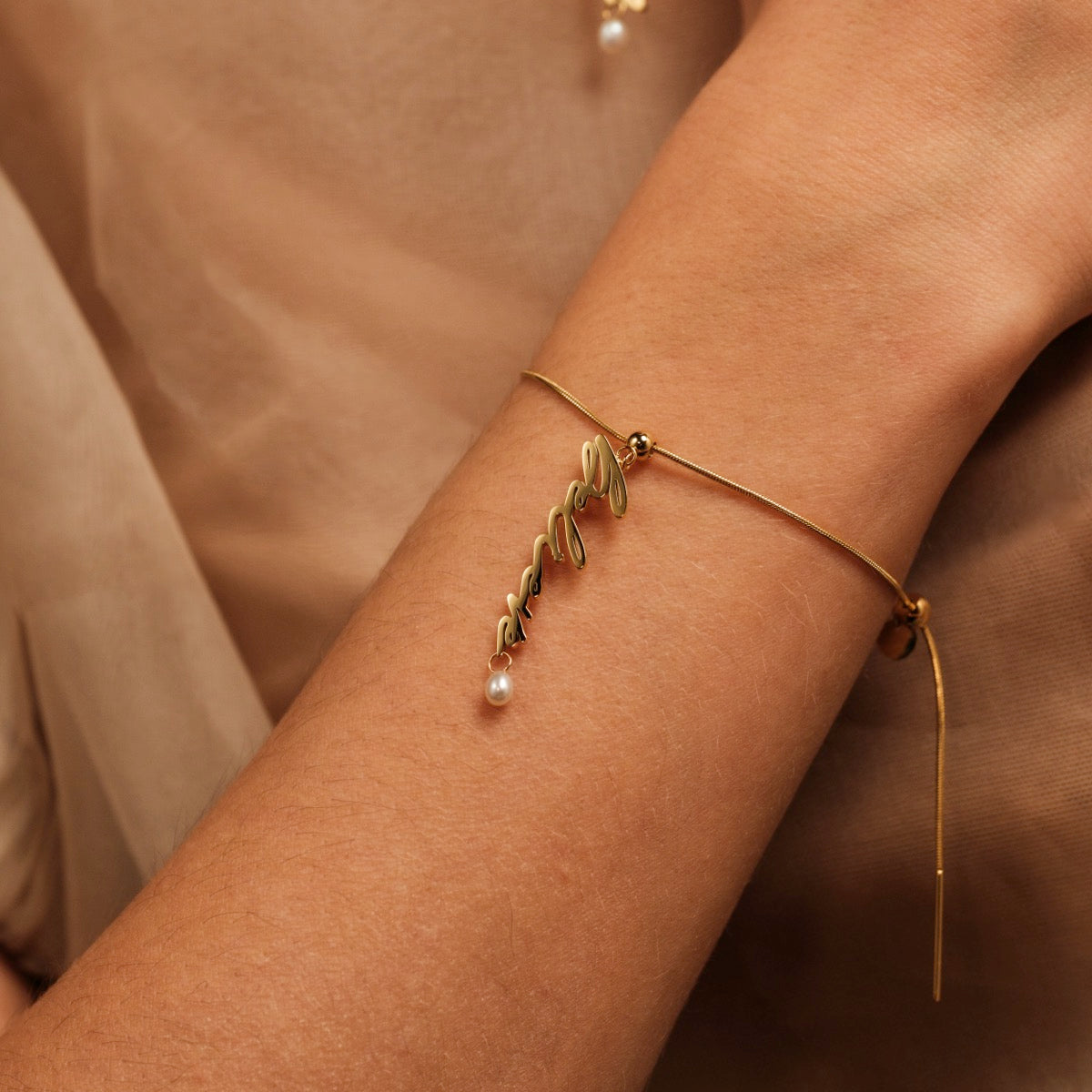 "Believe-Charm" bracelet featuring elegant gold lettering and a delicate pearl, styled on a wrist.