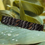 "Baritone" bracelet, featuring a sleek maple and black finish, elegantly showcased on green leaves with water droplets.