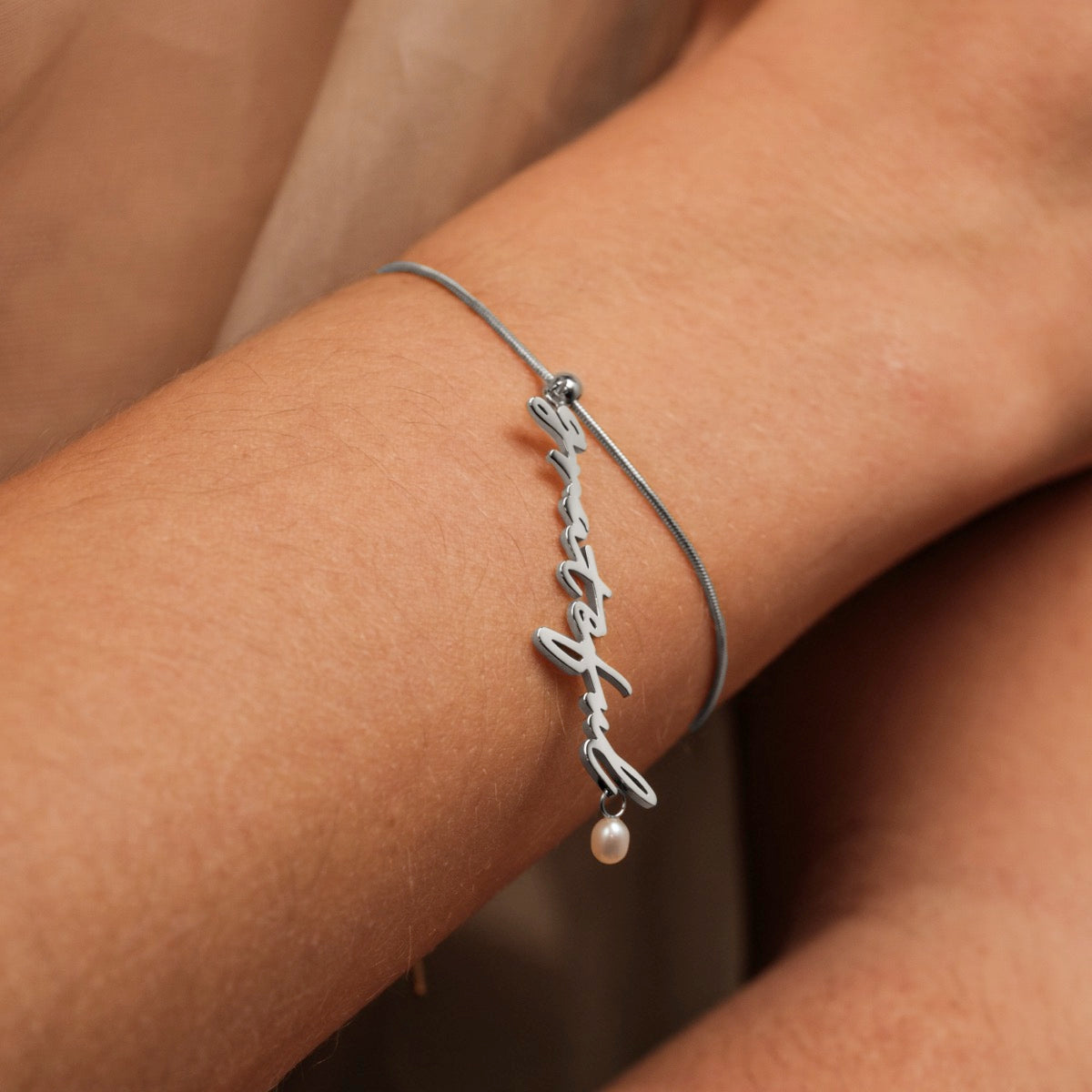 "Grateful-Charm" bracelet featuring elegant pearls and a silver charm with a minimalist design on the wrist.