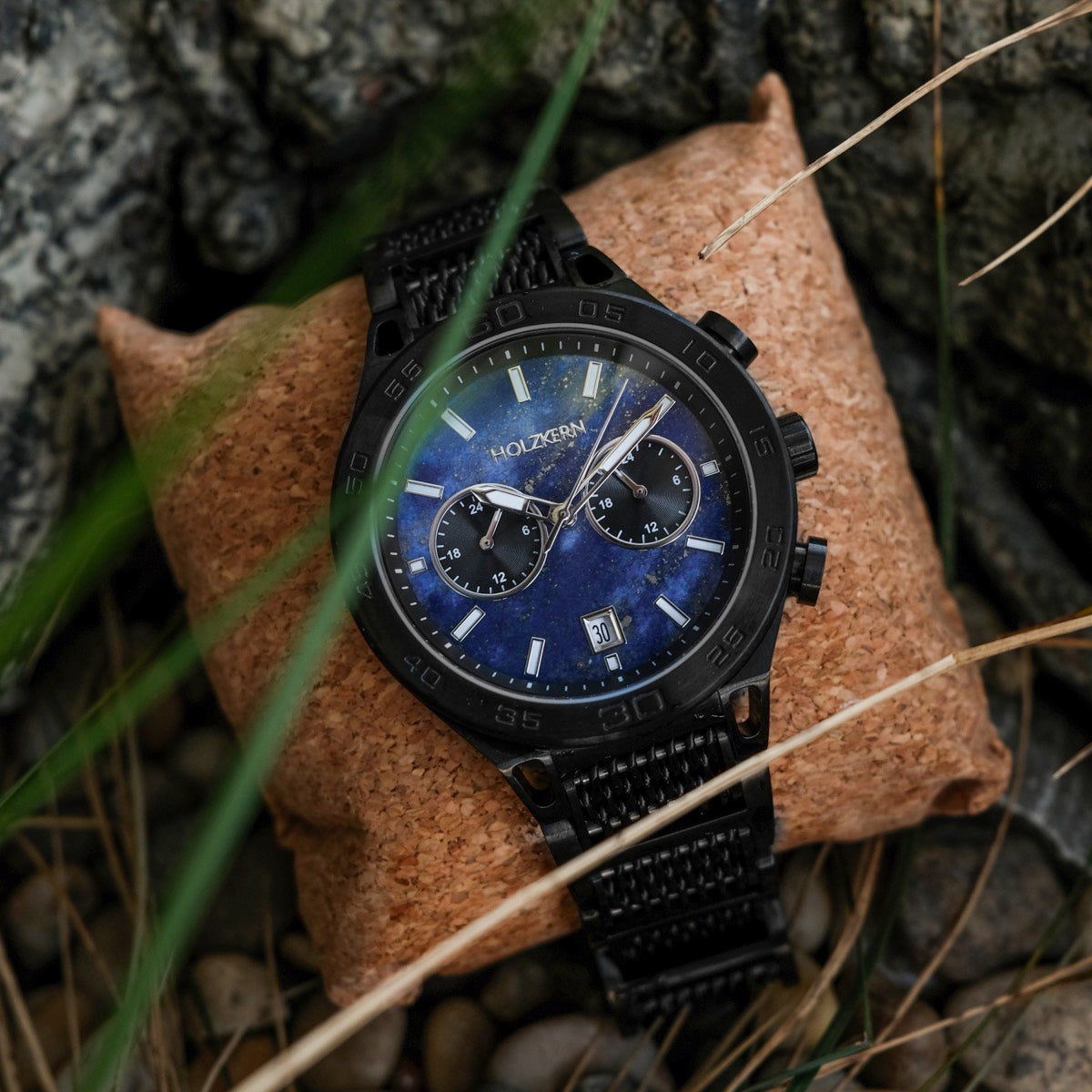 "Aoraki" watch features a striking Lapis Lazuli face and sleek black design, set against a natural background.