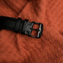 "Rackets belt featuring a sleek black buckle, styled on textured orange fabric."
