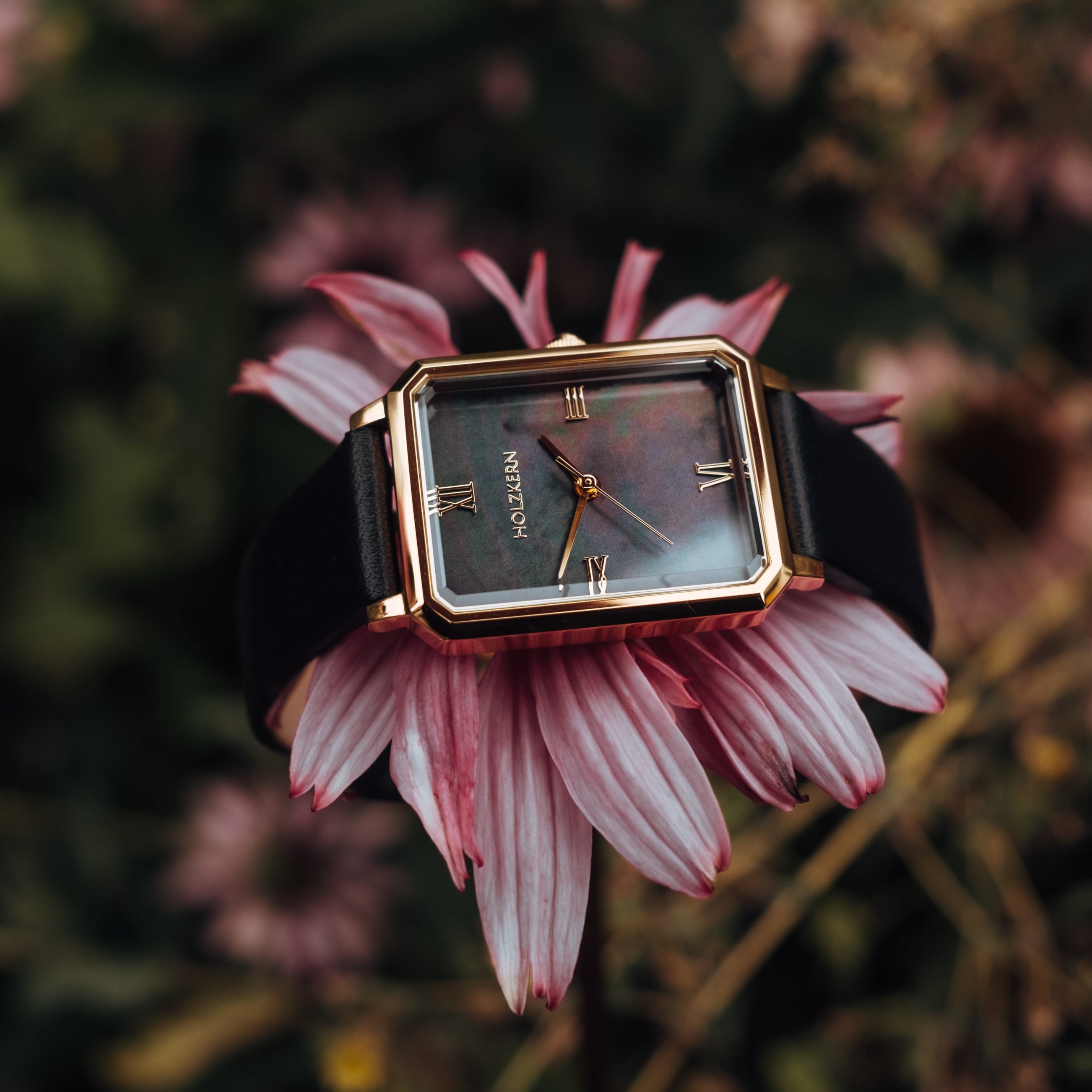 "Auctoritas" watch features a nacre dial and gold accents, elegantly displayed against a soft floral background.