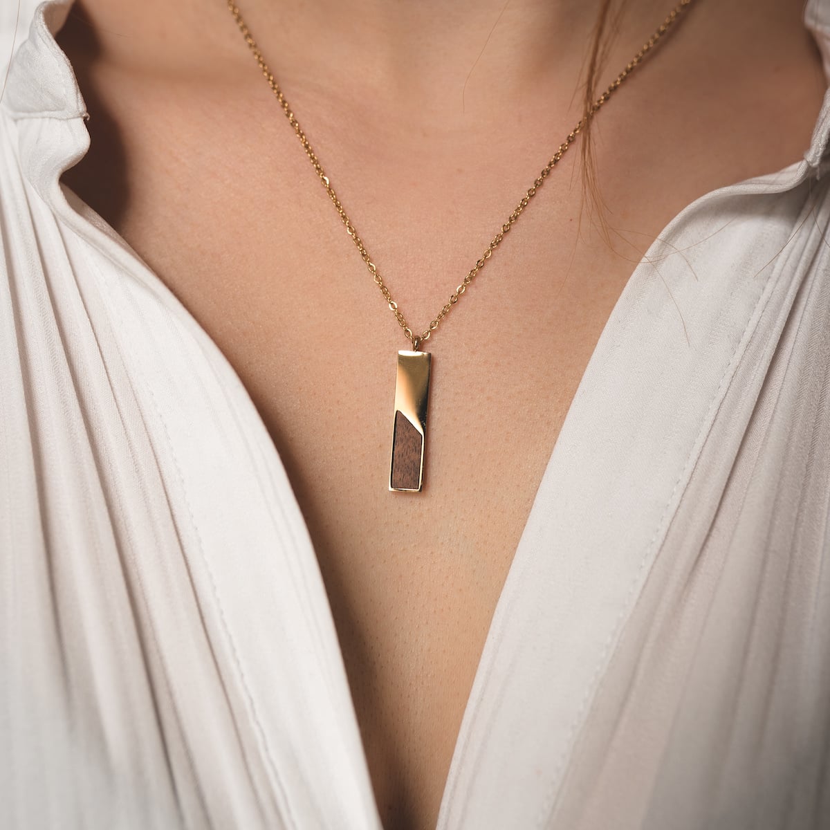 "Ephemera Necklace" necklace with a modern Koa wood and gold design displayed on a person in a white shirt.