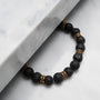 "Superset" bracelet featuring black lava beads and gold accents on a marble surface.
