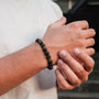 "Superset" bracelet featuring lava and gold beads, worn on a wrist with casual style.
