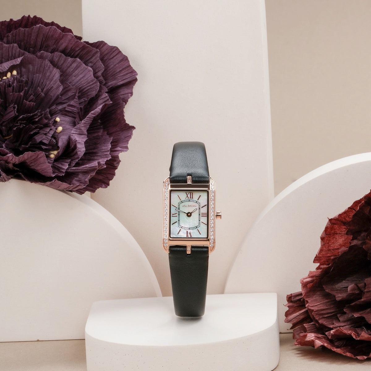 "Memoire", elegant watch with nacre dial and black band, surrounded by floral accents.