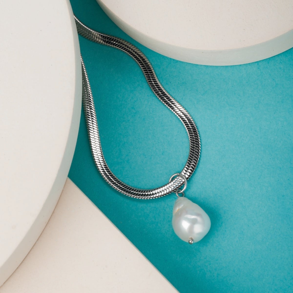 "Summersweet Necklace": a stylish necklace featuring a baroque pearl and silver design, set against a bright geometric backdrop.