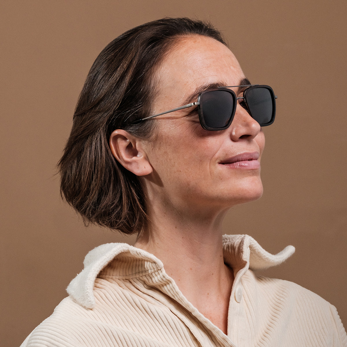 "The Logician" sunglasses featuring Leadwood/Antique Silver frame, worn by a woman with a neutral expression.