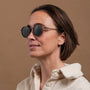 "The Radiant S" sunglasses feature a stylish walnut and copper design on a beige background.