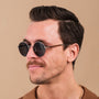 "The Adventurous" sunglasses featuring a walnut and dark gray color scheme with a stylish round frame design.