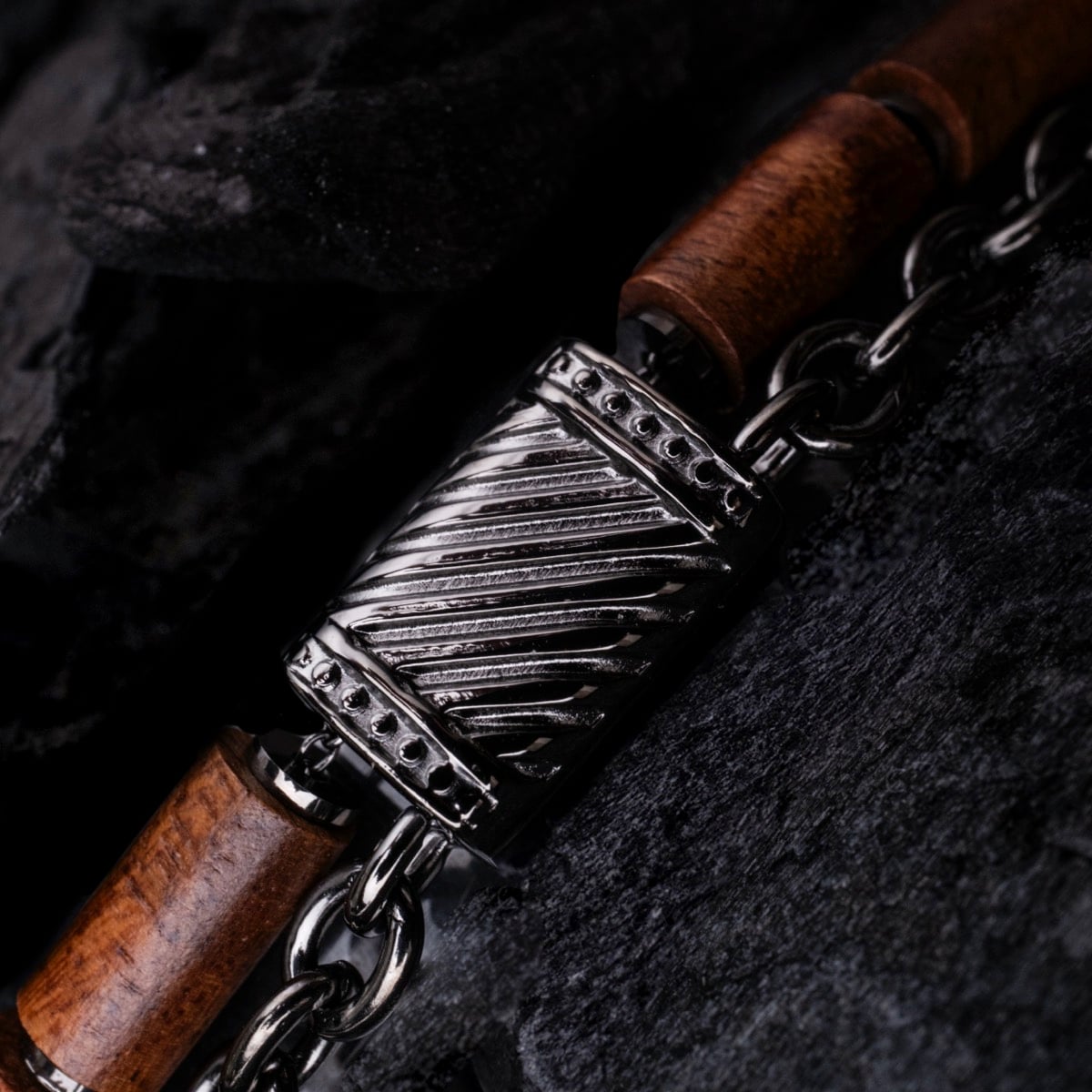 "Supersonic" bracelet featuring a koa wood and gray metal design against textured black rocks.