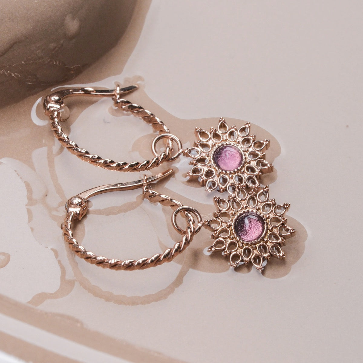 "Suncatcher Earrings", elegant earrings with an amethyst centerpiece and rose gold detailing, featuring a sunburst design.