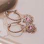 "Suncatcher Earrings", elegant earrings with an amethyst centerpiece and rose gold detailing, featuring a sunburst design.
