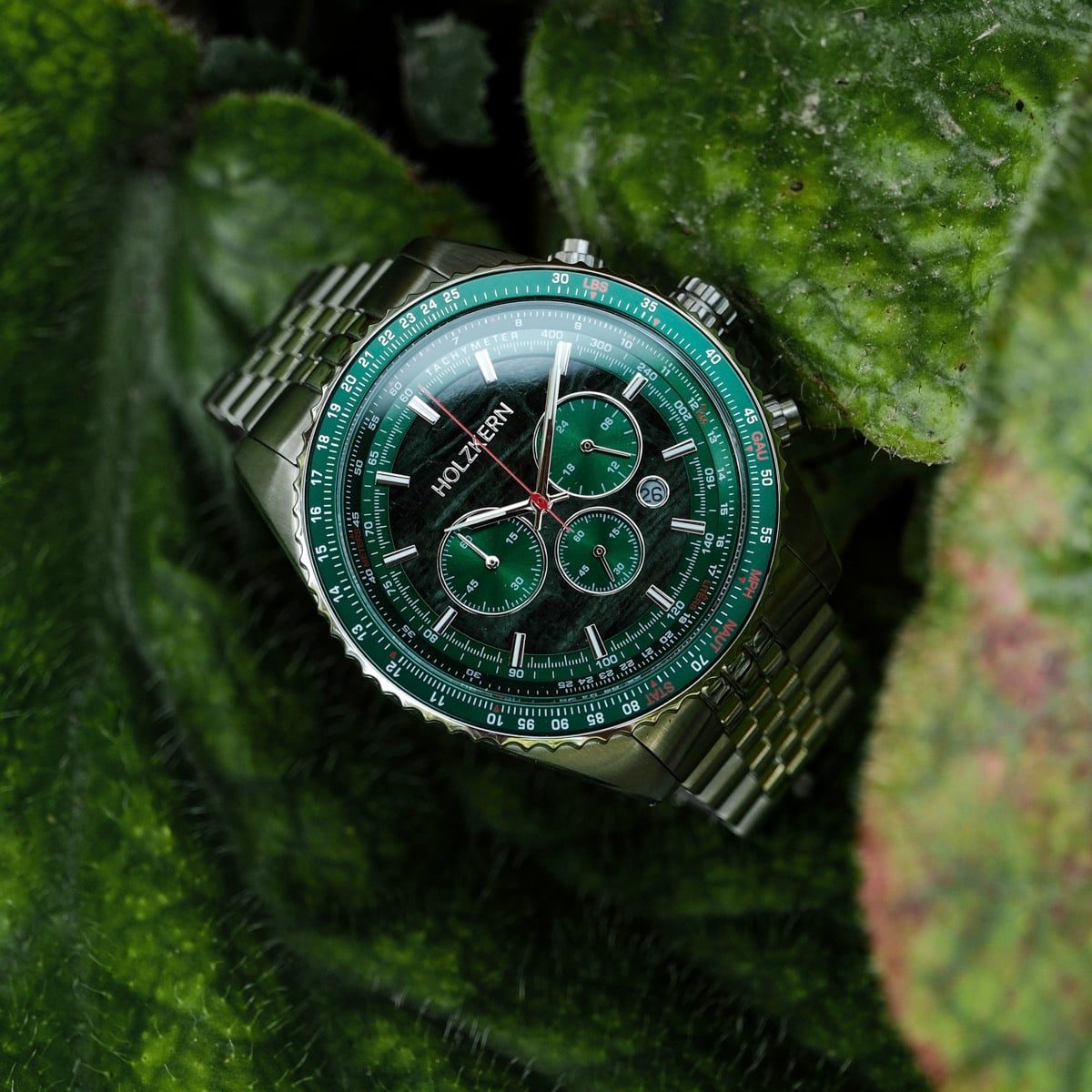 "Openhorizon" watch with a green marble dial and silver accents, displayed elegantly on leafy greenery.