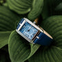 "Memoire" wristwatch features an elegant blue agate face and a refined band, set against lush green leaves.