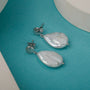 "Summersweet Earrings", elegant Baroque pearl and silver earrings on a vibrant turquoise background.
