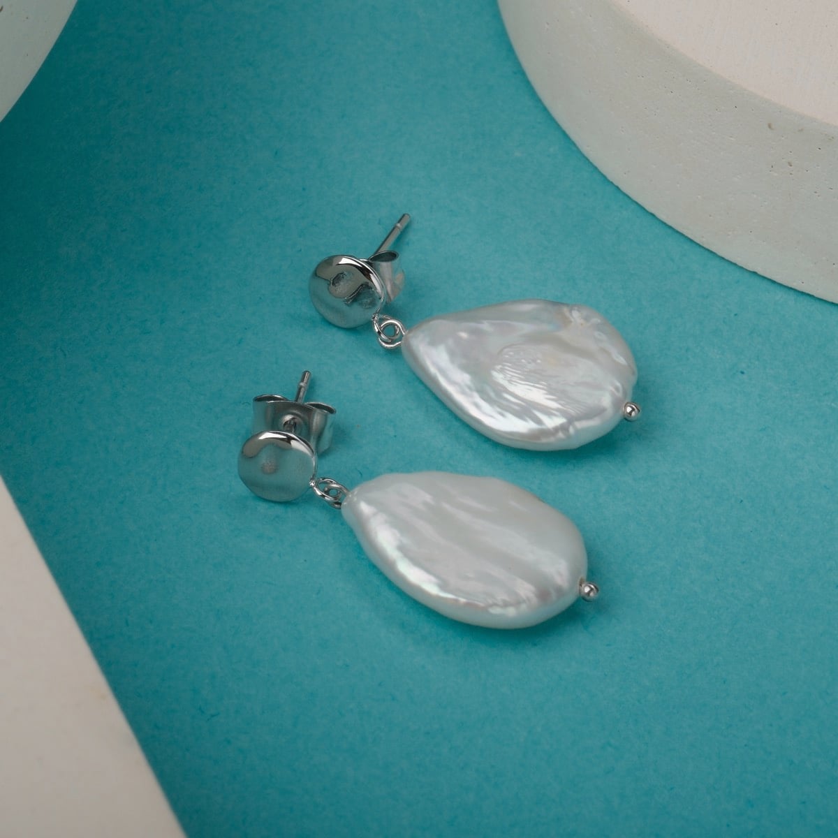 "Summersweet Earrings", elegant Baroque pearl and silver earrings on a vibrant turquoise background.