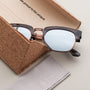 "The Virtuoso" sunglasses with a modern aesthetic, featuring Leadwood and Ash material accents, nestled in a cork case.