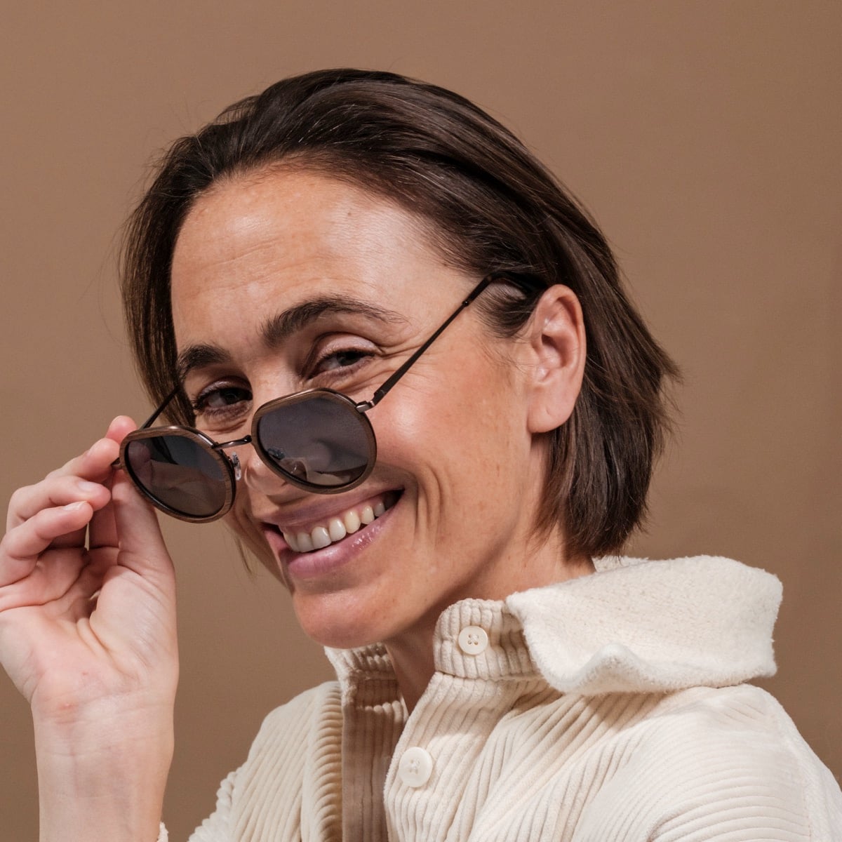 "The Wanderer" sunglasses in walnut/bronze style, worn by a smiling person against a neutral background.