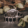 "Odaiba" watch with a maple/maple design, featuring a metallic and wood aesthetic in a natural setting.