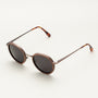 "The Radiant S" sunglasses featuring a walnut and copper finish with a modern, round design.