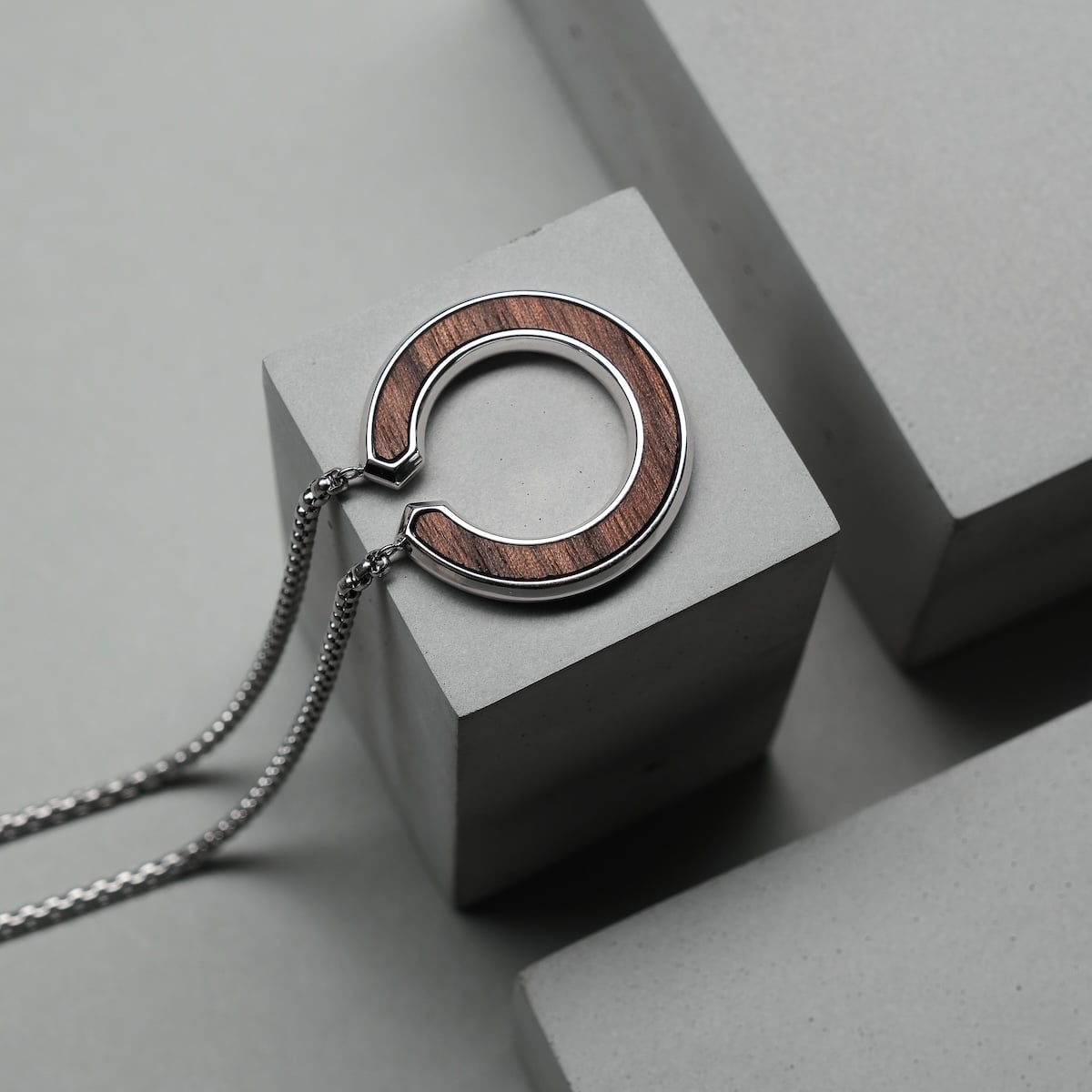 "Inseparable L" necklace, featuring a walnut and silver design, presented on a minimalist concrete background.