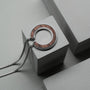 "Inseparable L" necklace, featuring a walnut and silver design, presented on a minimalist concrete background.