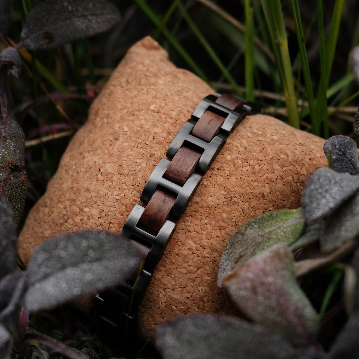 "Acoustic" bracelet, featuring a walnut and gray design, displayed on a textured cushion among foliage.