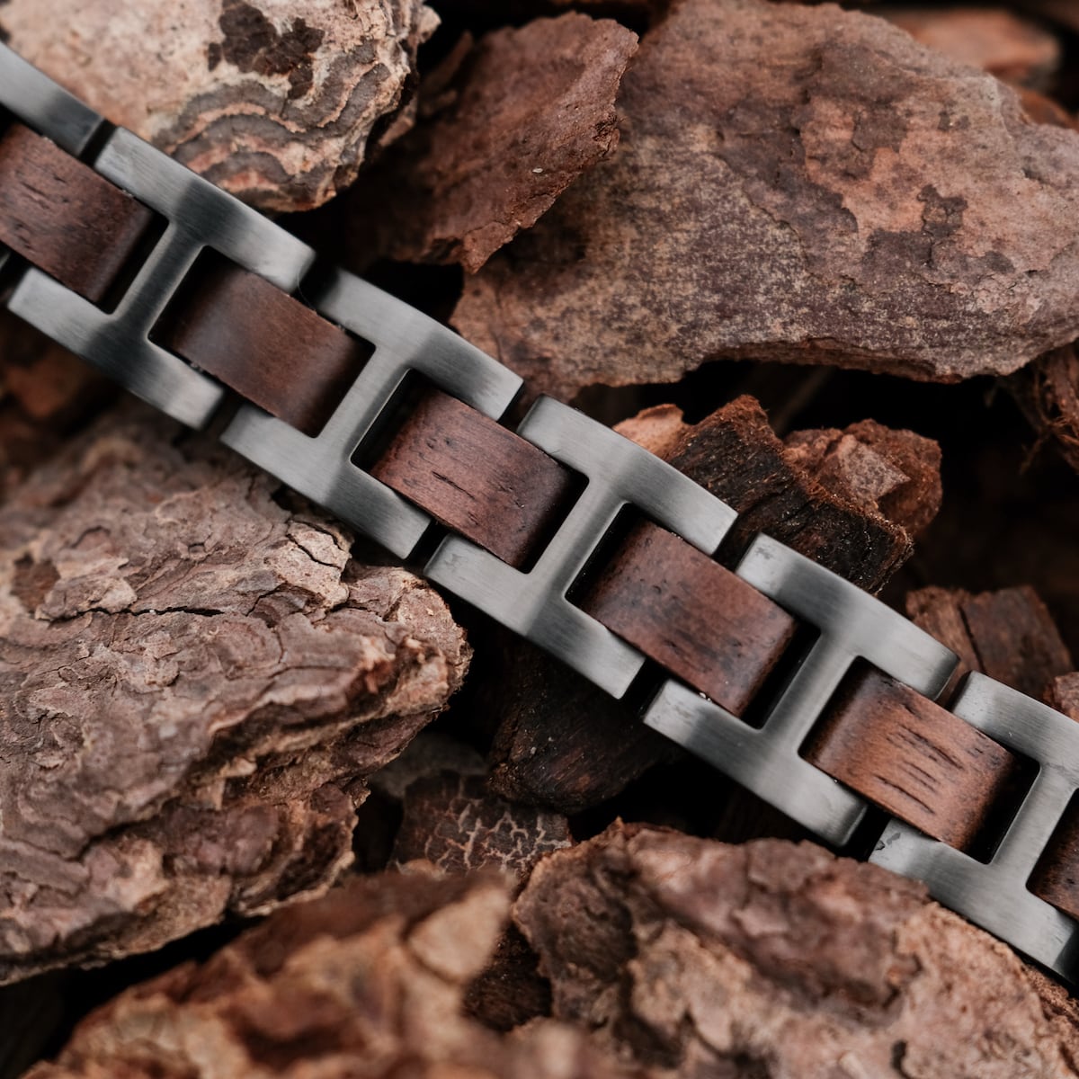 "Acoustic", a stylish bracelet with a walnut and gray metal design, resting on earthy bark.