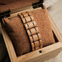 "Grandezza" watch with a maple and dark purple design, elegantly displayed on a cork cushion inside a wooden box.