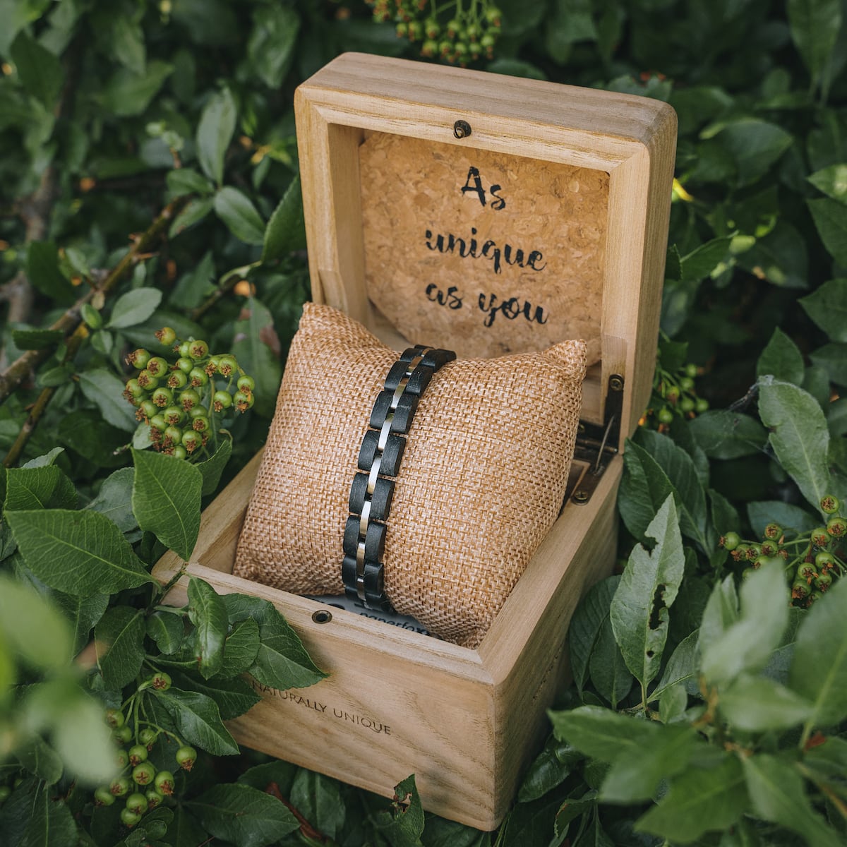 "Fantasia" bracelet in maple and silver, displayed in a rustic wooden box amidst greenery.