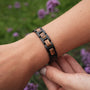 "Acoustic" bracelet, featuring a zebrawood and black design, worn on wrist amidst purple flowers.