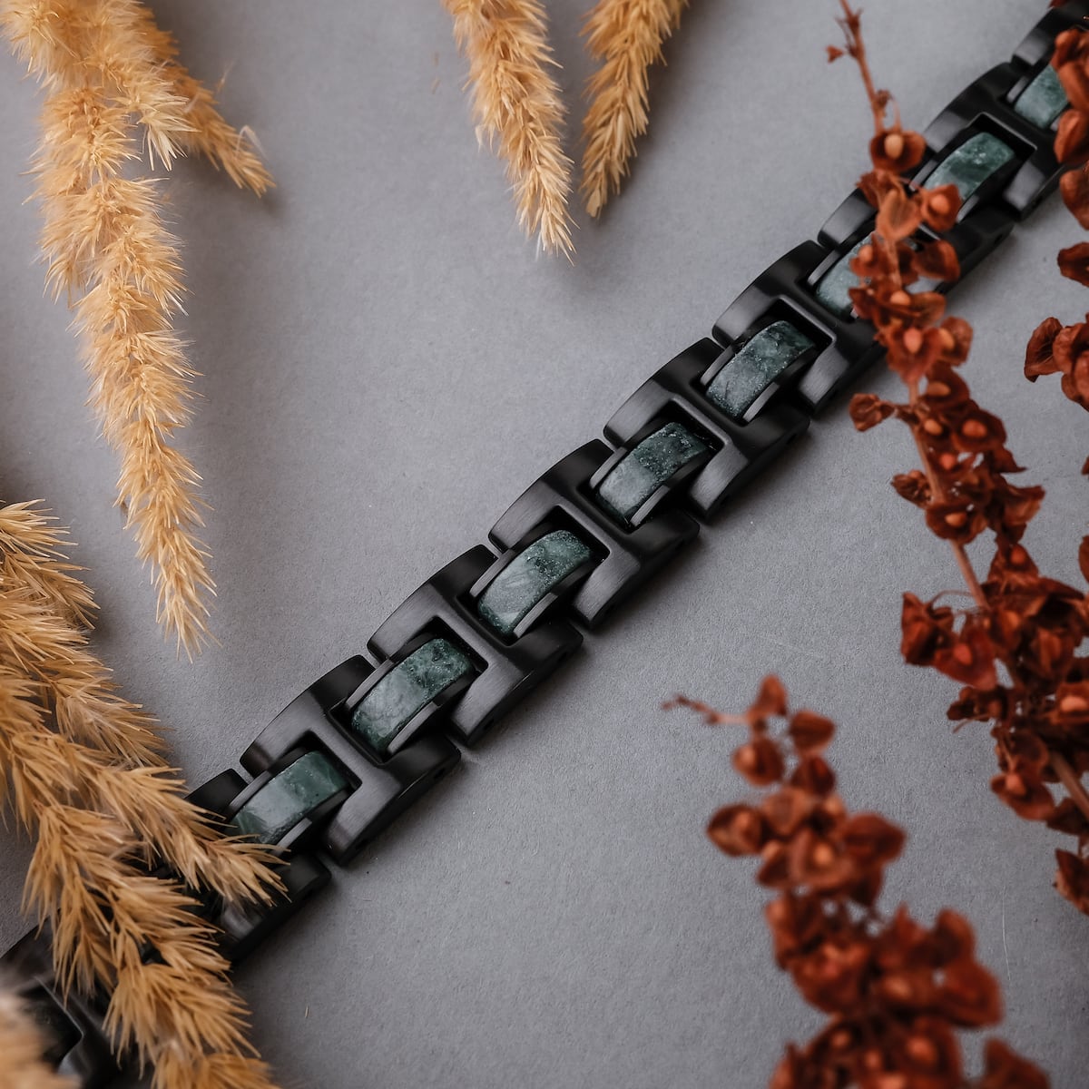 "Forte" bracelet with marble accents and black links, surrounded by rustic foliage.