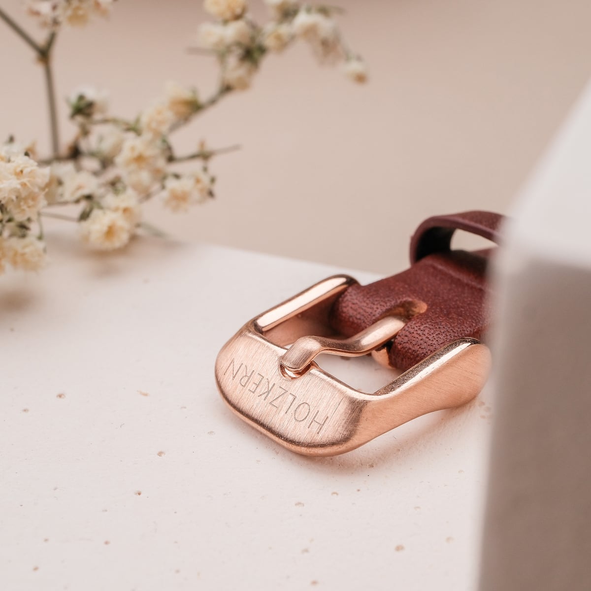 "Ida", a stylish belt buckle featuring walnut and marble aesthetics, set against a soft, floral background.