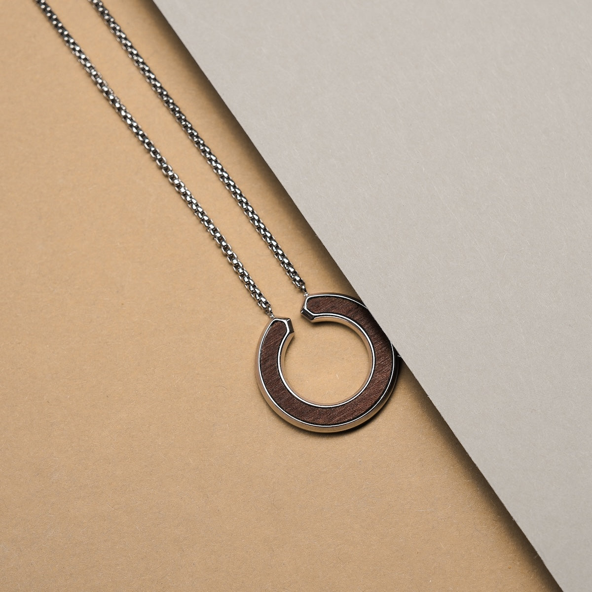 "Inseparable S" necklace featuring a walnut and silver design with a sleek circular pendant and chain.