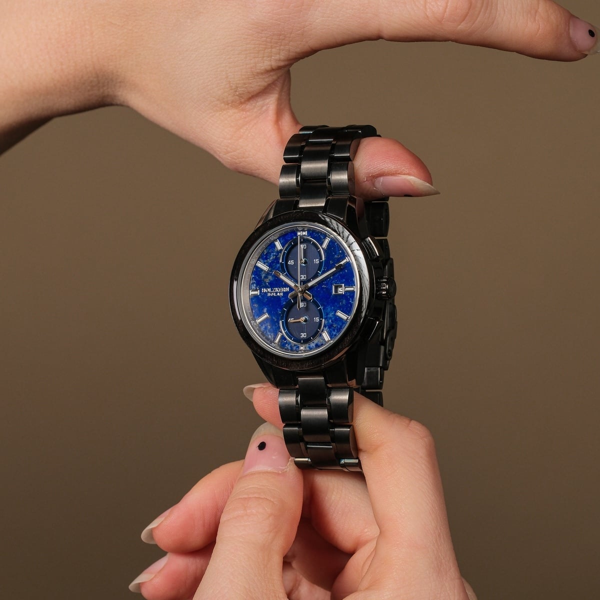 "Uplift" watch with a Lapis Lazuli dial and metal bracelet design, hero between two hands.